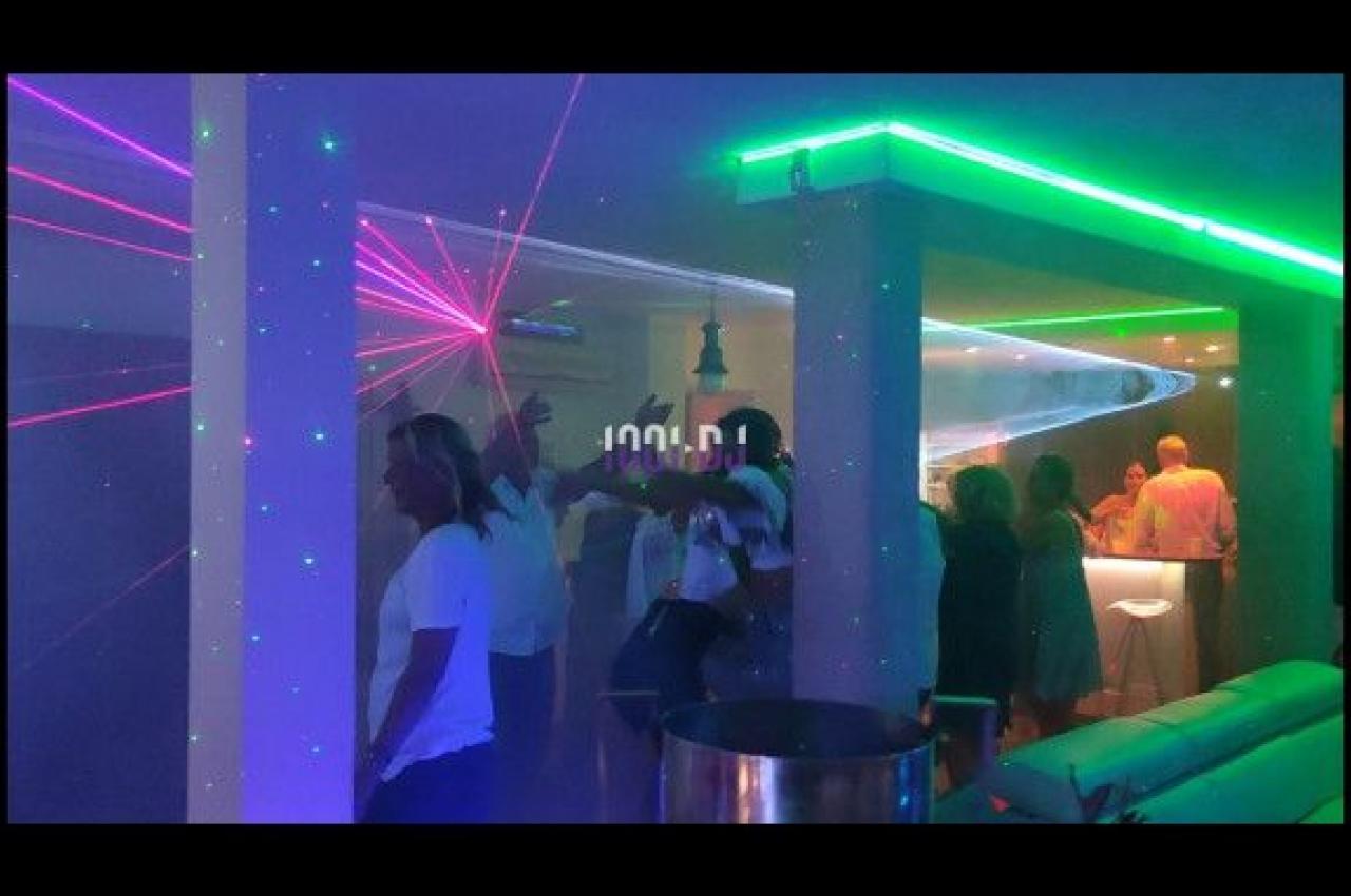 Des personnes dansent et discutent dans une salle éclairée par des lumières colorées et des lasers.