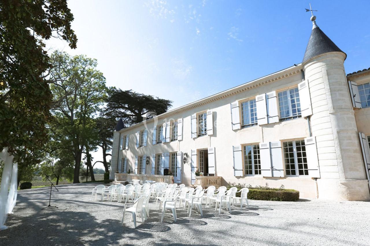 Façade d'un château avec des chaises blanches installées en extérieur, entouré d'arbres et baigné de lumière naturelle.