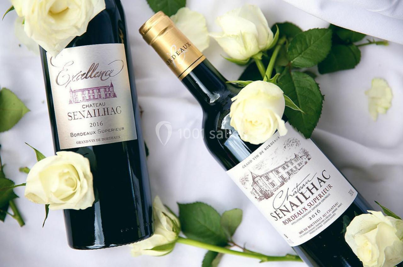 Deux bouteilles de vin rouge Château Senailhac entourées de roses blanches sur un fond clair.