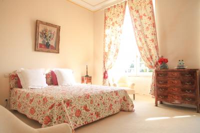 Chambre lumineuse avec murs en toile de Jouy rouge, mobilier classique, table basse et fauteuils près d'une fenêtre.