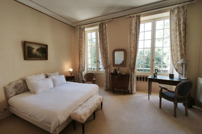 Chambre lumineuse avec murs en toile de Jouy rouge, mobilier classique, table basse et fauteuils près d'une fenêtre.