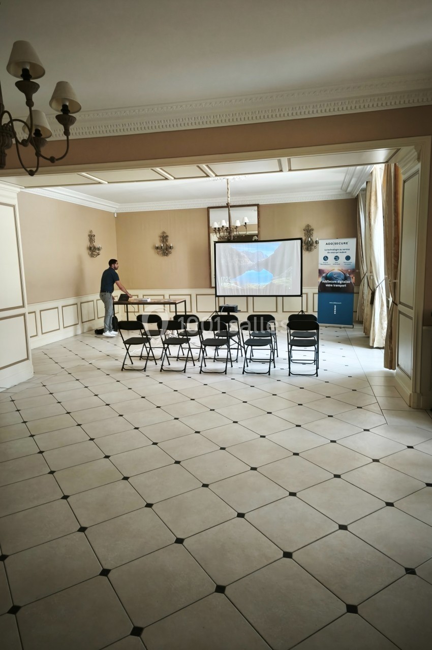 Salle de conférence lumineuse avec des chaises alignées, un écran de projection et une personne ajustant l'équipement.