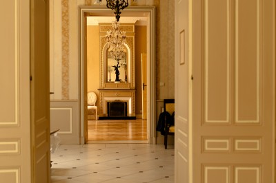 Façade claire avec volets blancs, lanterne en fer forgé et jardinières de fleurs roses en premier plan.