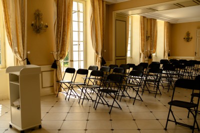 Façade claire avec volets blancs, lanterne en fer forgé et jardinières de fleurs roses en premier plan.