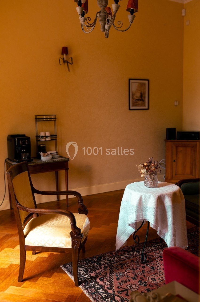 Salon lumineux avec fauteuil en bois, table ronde recouverte d'une nappe blanche et décoration sobre.