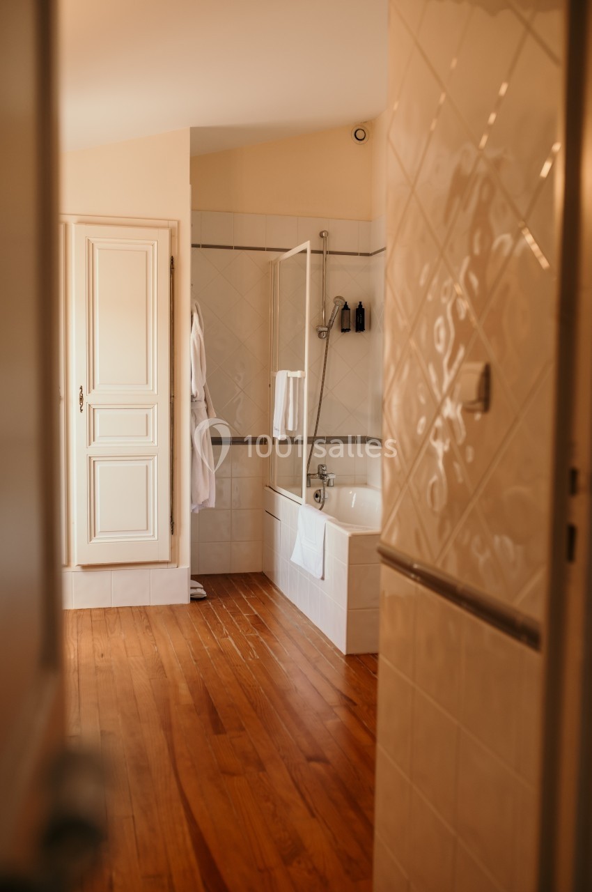 Salle de bain lumineuse avec baignoire, paroi vitrée, peignoirs accrochés et sol en bois.