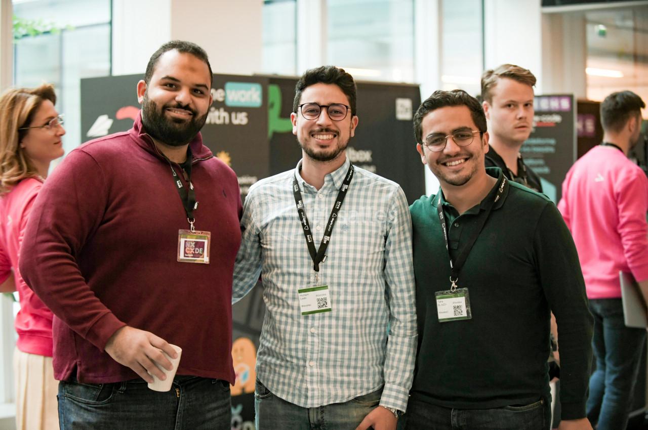 Trois hommes souriants posent ensemble dans un espace professionnel lors d'un événement, badges autour du cou.