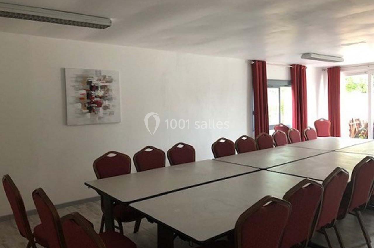 Salle de réunion lumineuse avec une grande table rectangulaire entourée de chaises rouges et un tableau décoratif au mur.