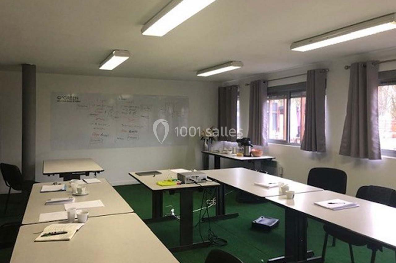 Salle de réunion lumineuse avec tables disposées en U, tableau blanc au mur et matériel de travail sur les tables.