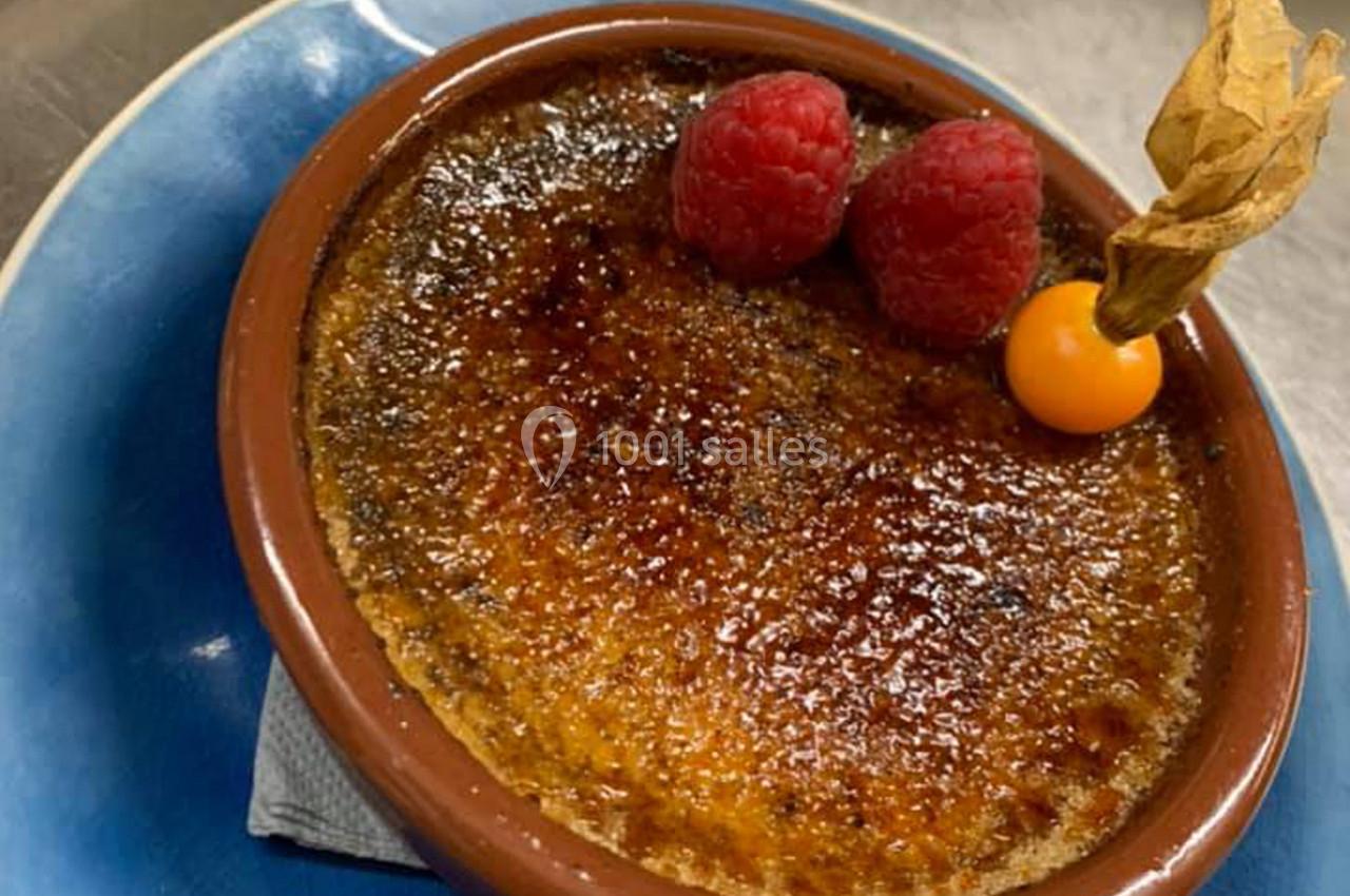 Crème brûlée dorée servie dans un ramequin, décorée de framboises et d'un physalis sur une assiette bleue.