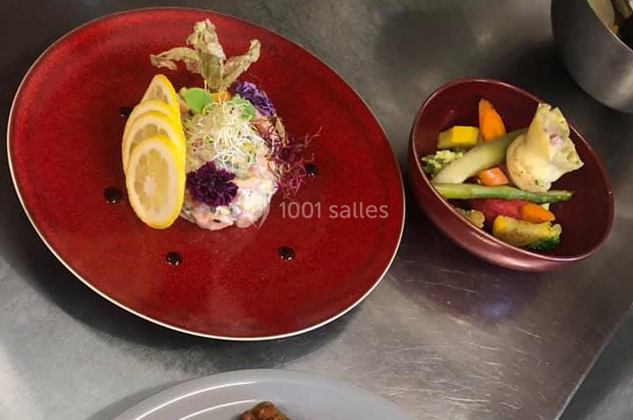 Assiette de tartare décorée de citron et fleurs comestibles, accompagnée de légumes variés dans un bol.