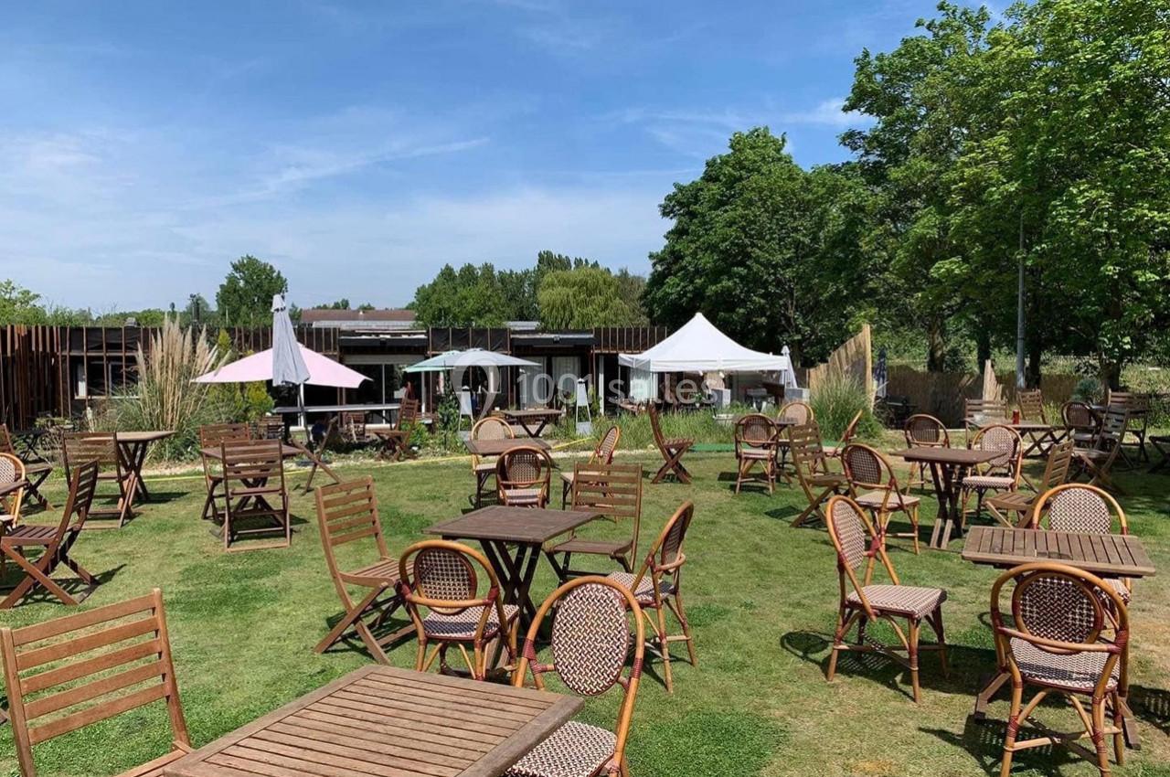 Location salle Hem (Nord) - O'Green du Château d'Hem #7 Chaises et tables en bois disposées sur une pelouse, entourées de végétation et de tentes blanches sous un ciel dégagé.