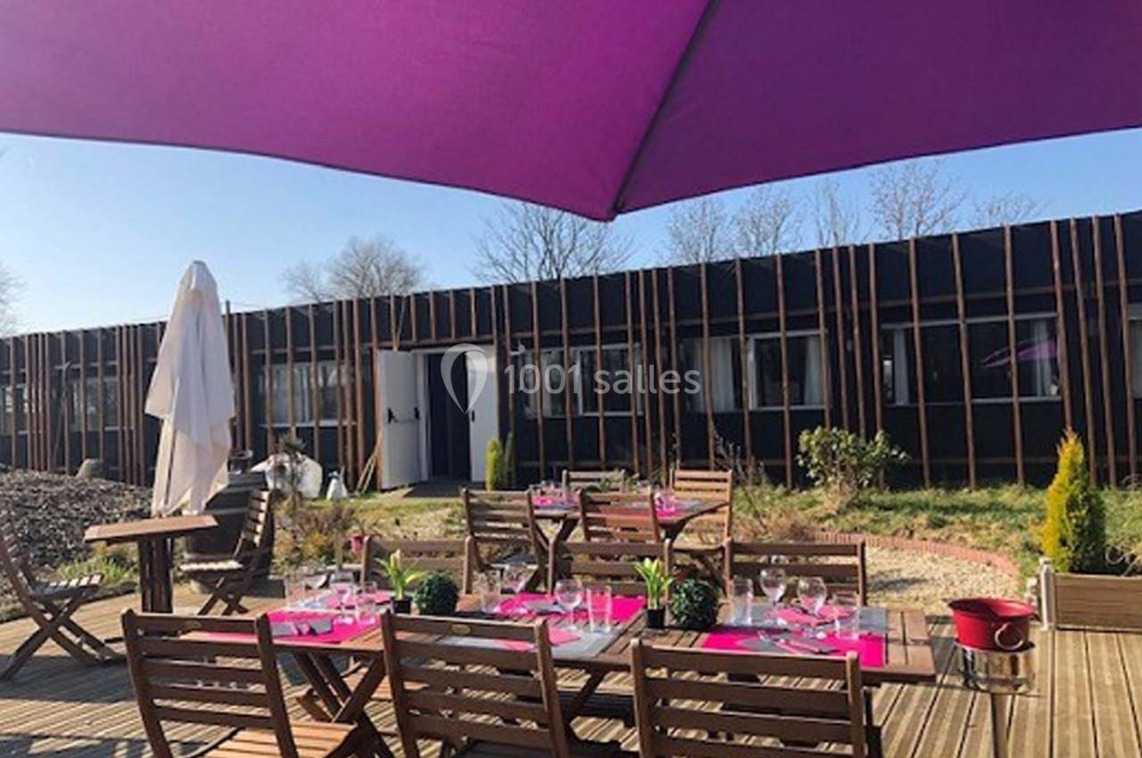 Location salle Hem (Nord) - O'Green du Château d'Hem #10 Terrasse en bois avec tables et chaises en bois, dressées pour un repas, sous un grand parasol violet.