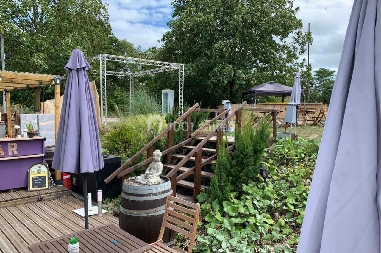 Location salle Hem (Nord) - O'Green du Château d'Hem #32 Terrasse extérieure avec tables, parasols, statue décorative et végétation, surplombant un espace verdoyant.