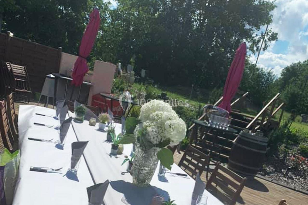 Location salle Hem (Nord) - O'Green du Château d'Hem #38 Table dressée en extérieur avec nappes blanches, fleurs en centre de table, parasols roses et verdure en arrière-plan.