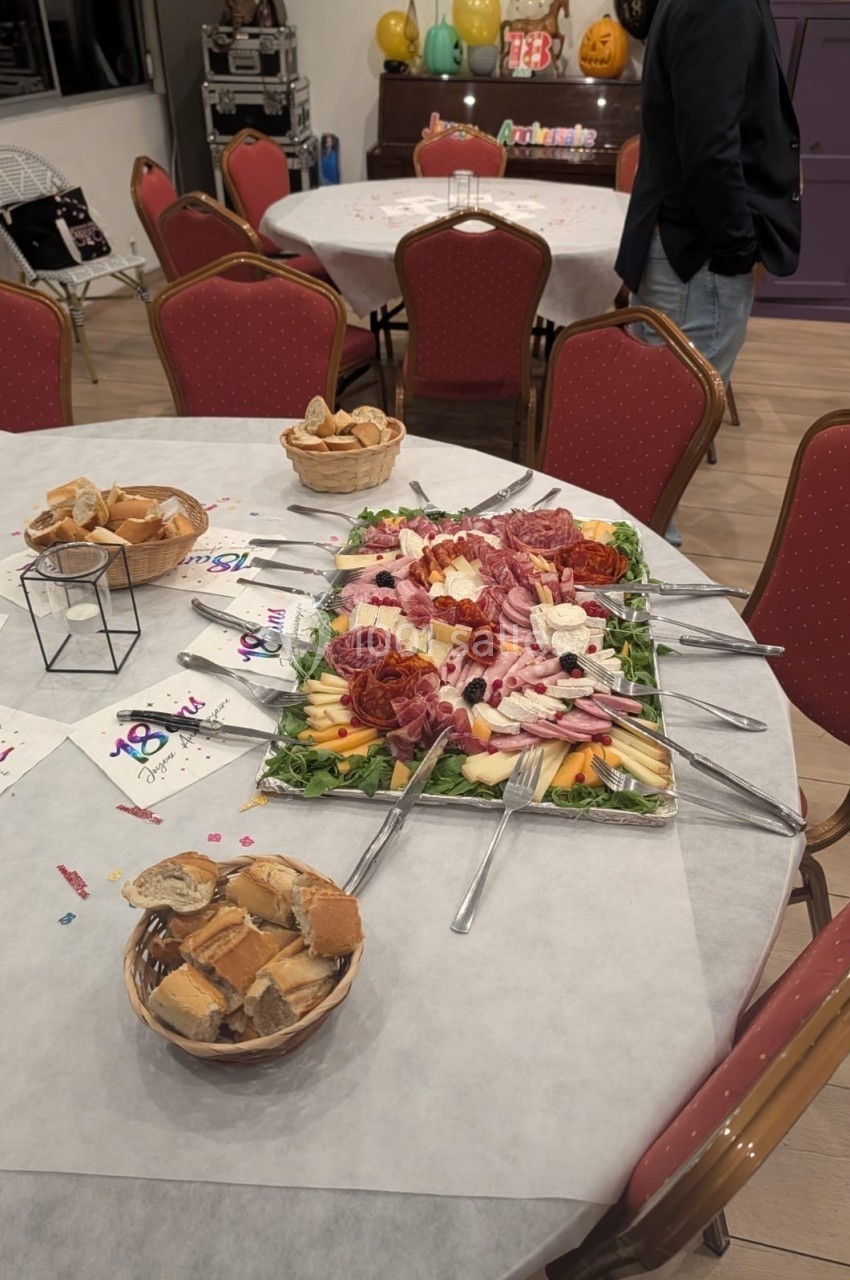 Location salle Hem (Nord) - O'Green du Château d'Hem #54 Plateau de charcuterie et fromages décoré avec fruits, entouré de couverts, sur une table dressée avec paniers de pain.