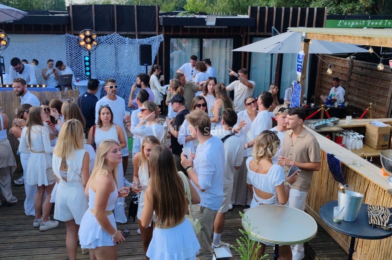 Location salle Hem (Nord) - O'Green du Château d'Hem #2 Groupe de personnes en tenue estivale blanche réunies sur une terrasse en bois lors d'un événement en plein air.