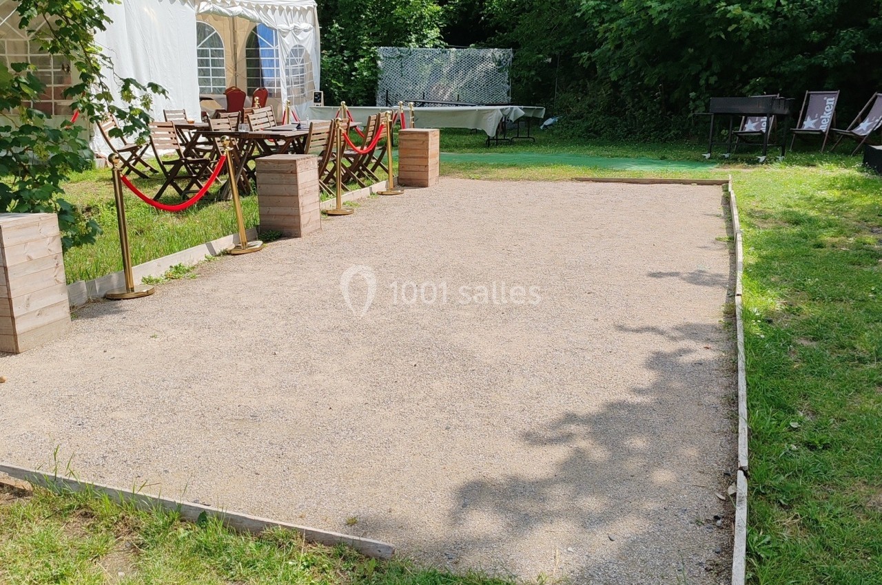 Location salle Hem (Nord) - O'Green du Château d'Hem #55 Terrain de pétanque en gravier entouré de verdure, avec des tables et une tente blanche en arrière-plan.