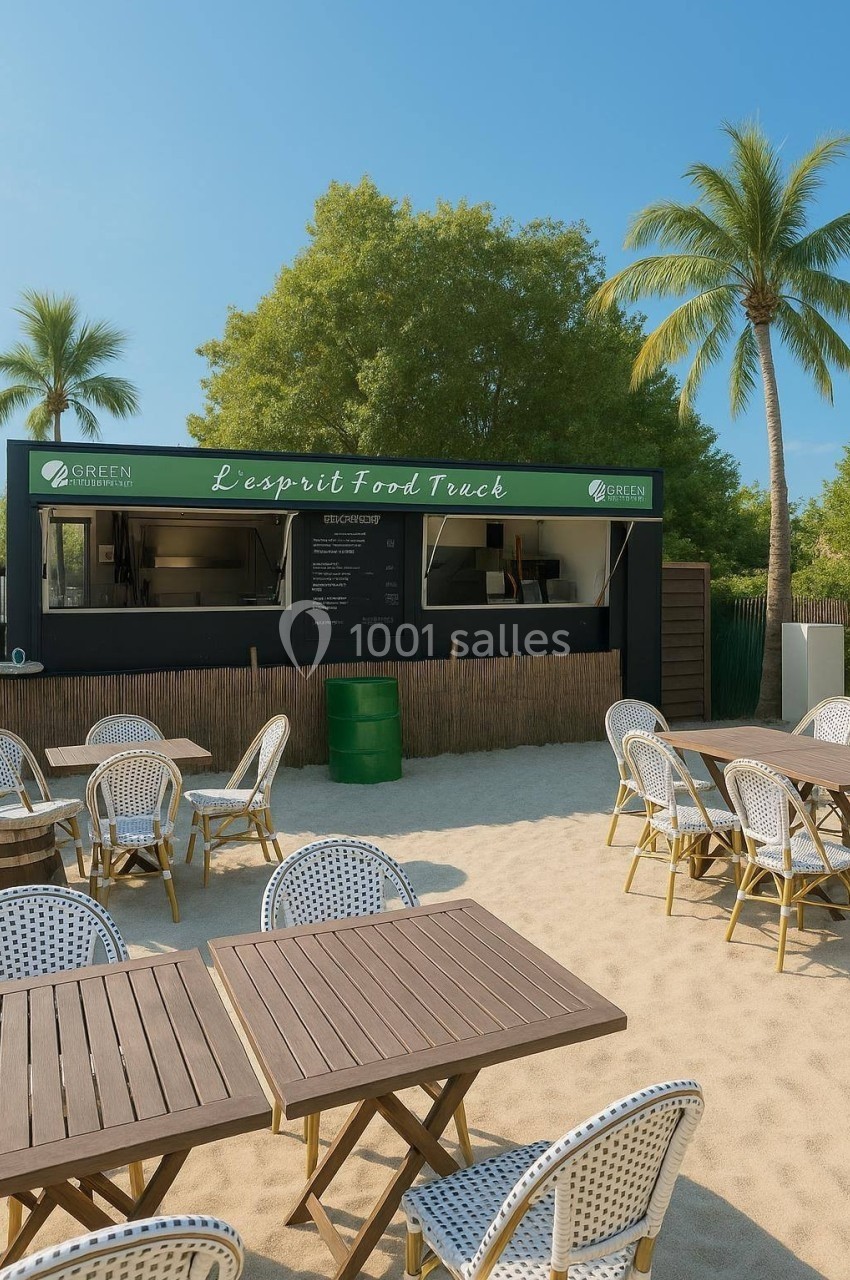 Location salle Hem (Nord) - O'Green du Château d'Hem #12 Food truck sur une plage avec des tables et chaises en rotin, entouré de palmiers et d'arbres sous un ciel dégagé.
