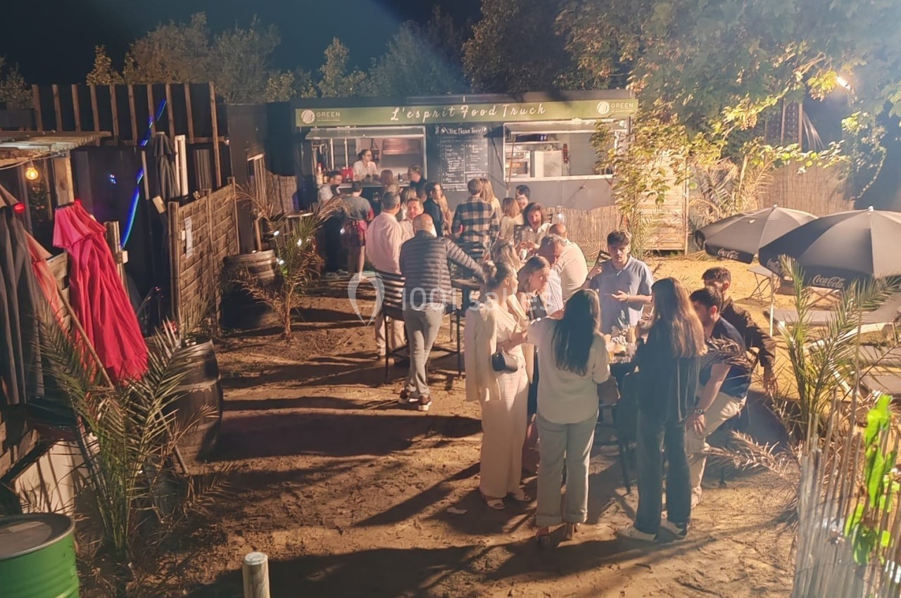 Location salle Hem (Nord) - O'Green du Château d'Hem #13 Groupe de personnes rassemblées en soirée devant un food truck, entouré de végétation et éclairé par des lumières.