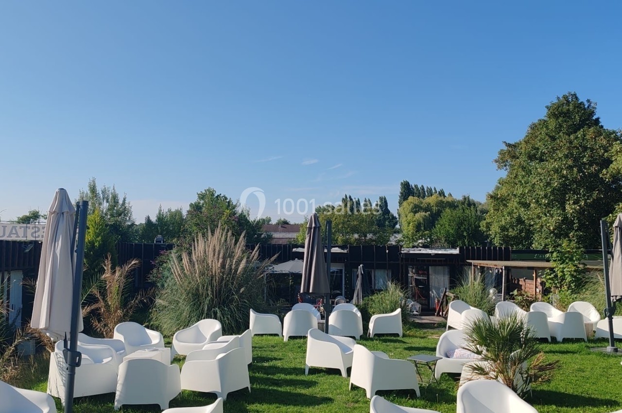 Location salle Hem (Nord) - O'Green du Château d'Hem #4 Chaises blanches et parasols disposés sur une pelouse, entourés de végétation et sous un ciel dégagé.