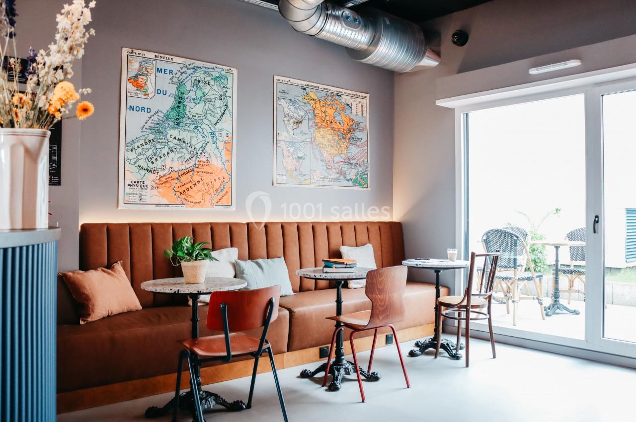 Banquette en cuir marron avec tables et chaises, décorée de cartes murales, près d'une baie vitrée donnant sur une terrasse.
