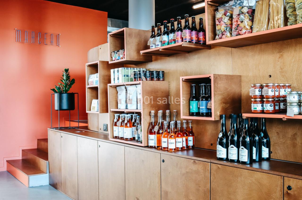 Étagères en bois avec bouteilles, bocaux, et produits alimentaires exposés dans un espace au mur orange.