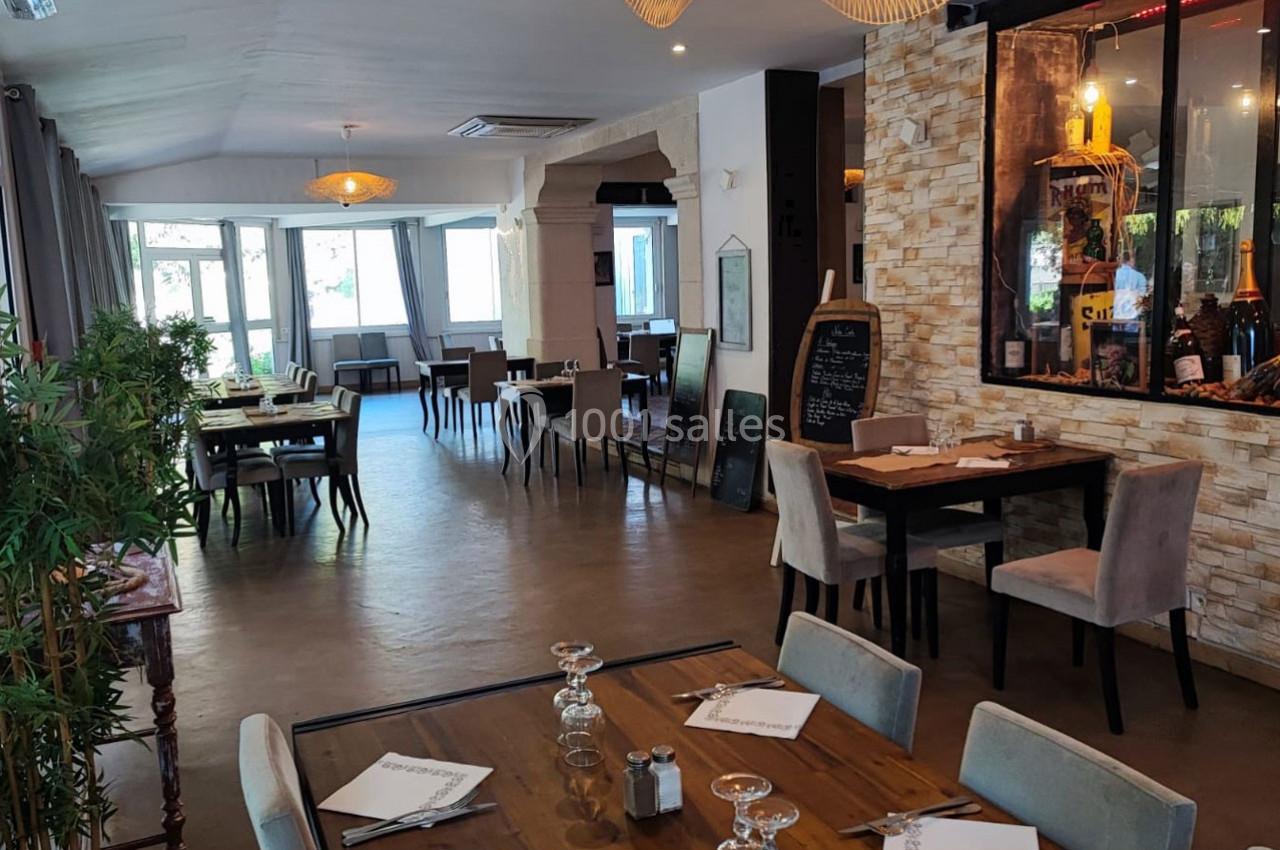 Salle de restaurant lumineuse avec tables dressées, décoration moderne et murs en pierre apparente.