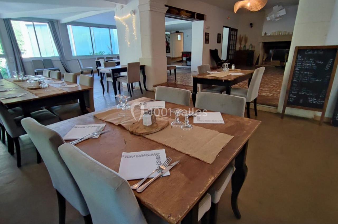 Salle de restaurant lumineuse avec tables en bois dressées, nappes en toile de jute et ardoise de menu au fond.
