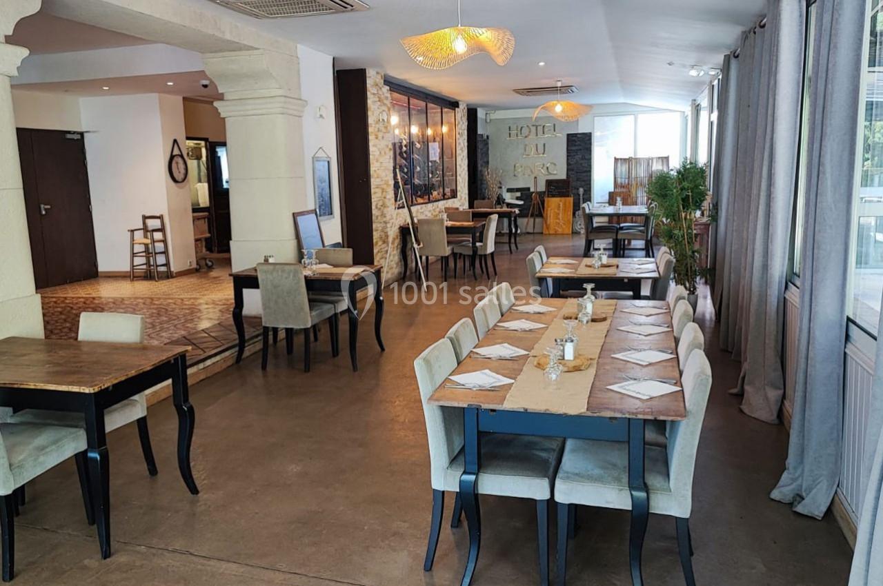 Salle de restaurant lumineuse avec tables dressées, chaises rembourrées et décor sobre mêlant pierre et bois.