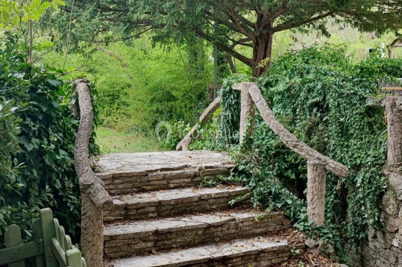 Escalier en pierre bordé de rampes en bois, entouré de végétation dense et d'arbres.