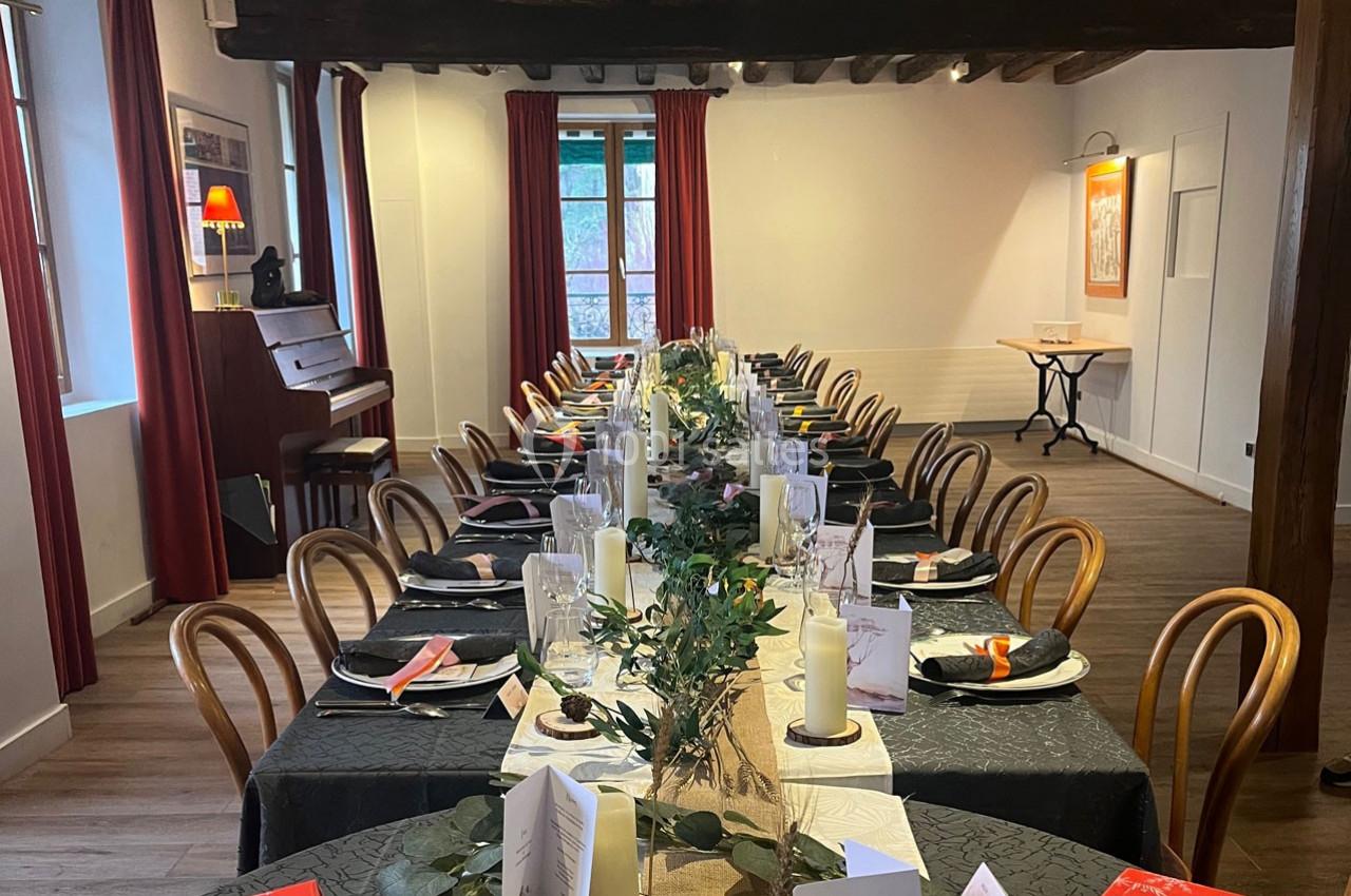 Salle à manger décorée avec une longue table dressée, nappes noires, bougies et éléments végétaux, piano en arrière-plan.