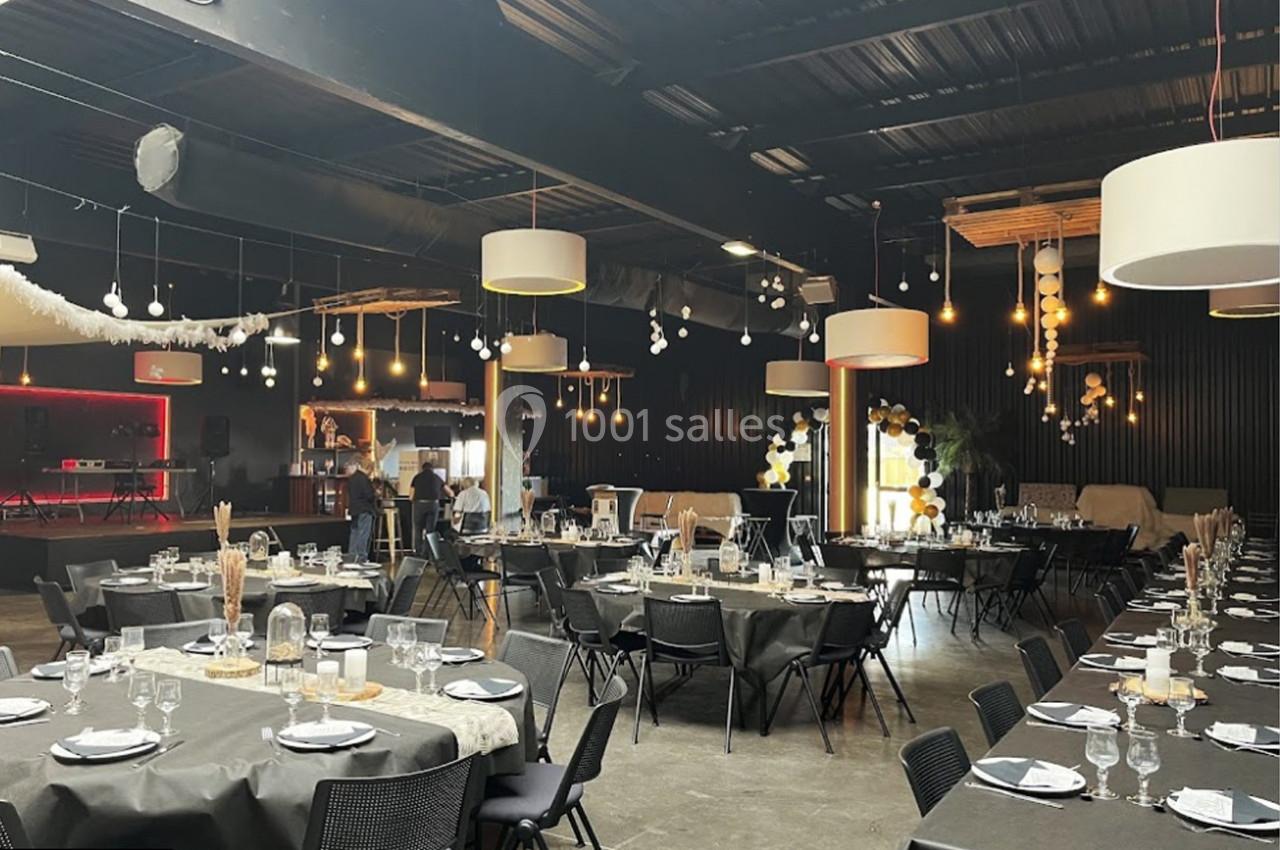 Salle de réception décorée avec des tables dressées, des guirlandes lumineuses et un bar en arrière-plan.