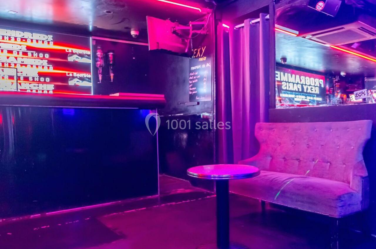 Banquette et table basse dans un espace intérieur sombre éclairé par des néons roses et violets.