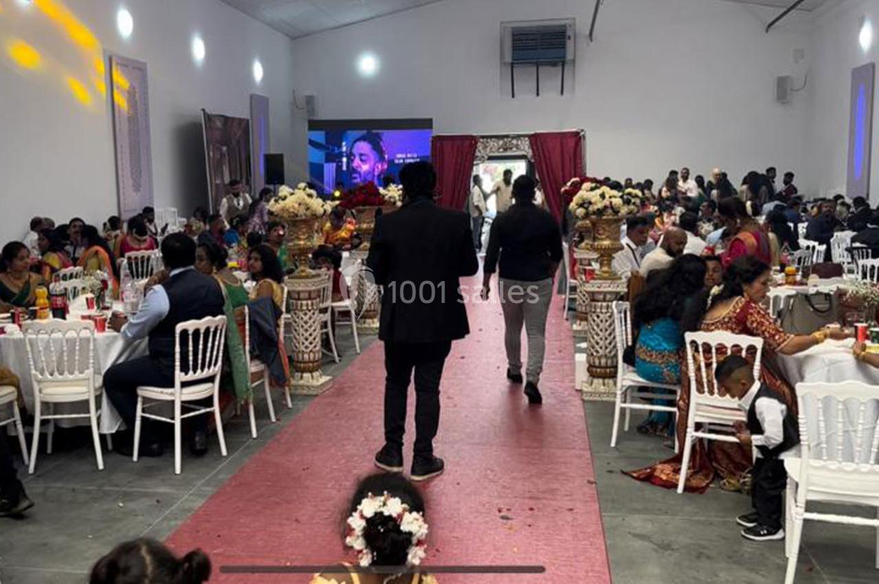 Salle de réception décorée, avec des invités assis à des tables rondes et un écran diffusant une vidéo en arrière-plan.
