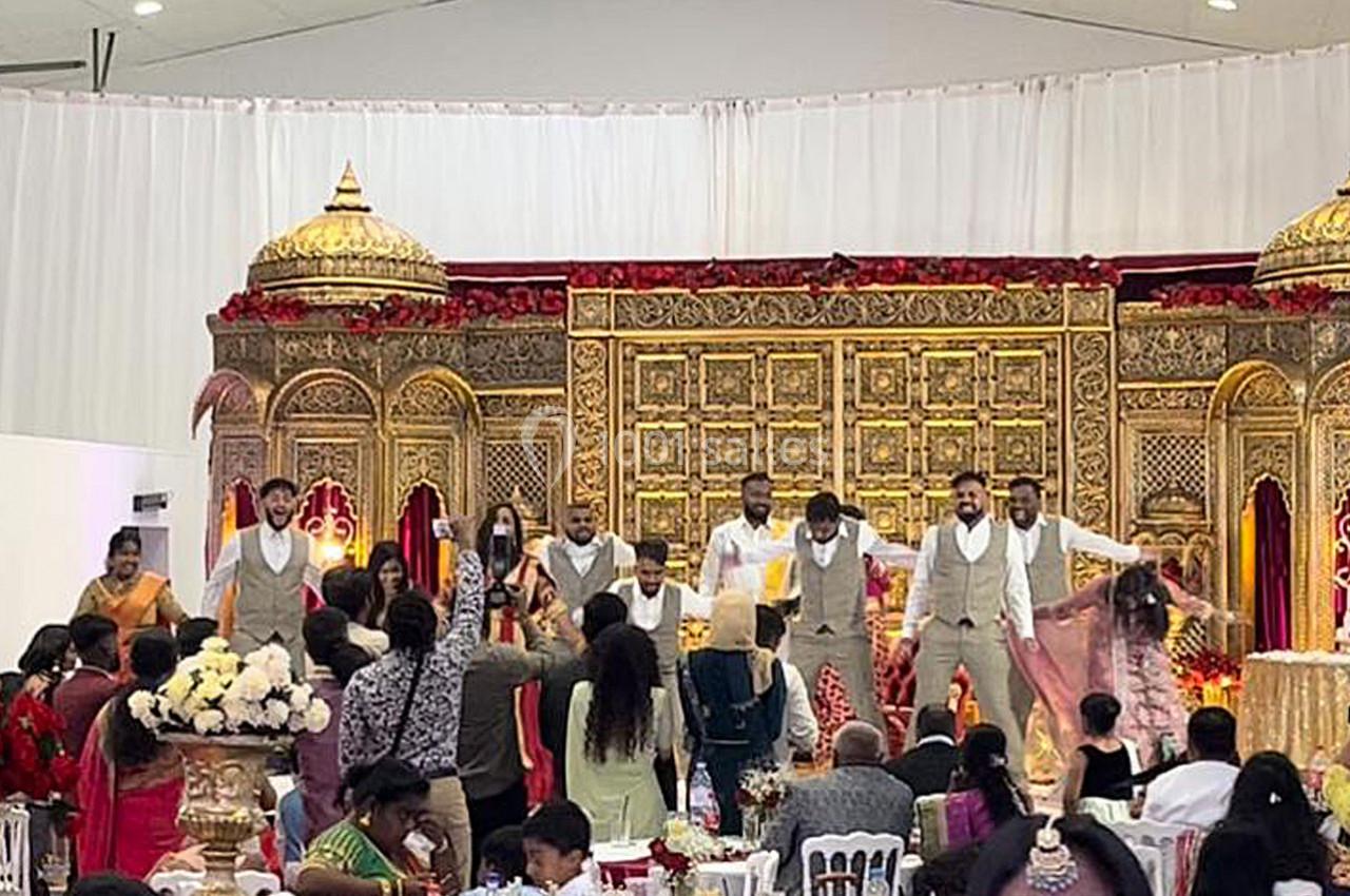 Des invités assistent à une danse festive sur une scène ornée de décorations dorées lors d'une célébration.