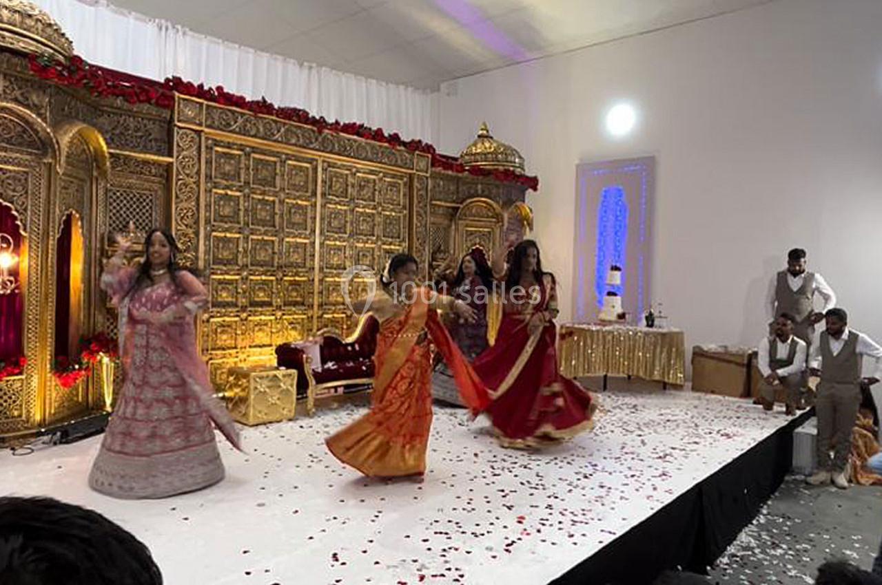 Des femmes en tenues traditionnelles dansent sur une scène décorée de motifs dorés et de pétales de fleurs.