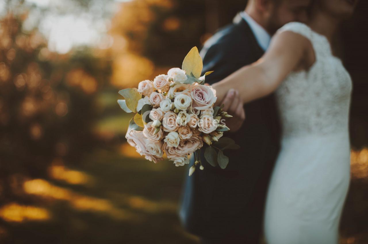 Un couple de mariés dans un jardin, la mariée tenant un bouquet de roses pastel au premier plan.