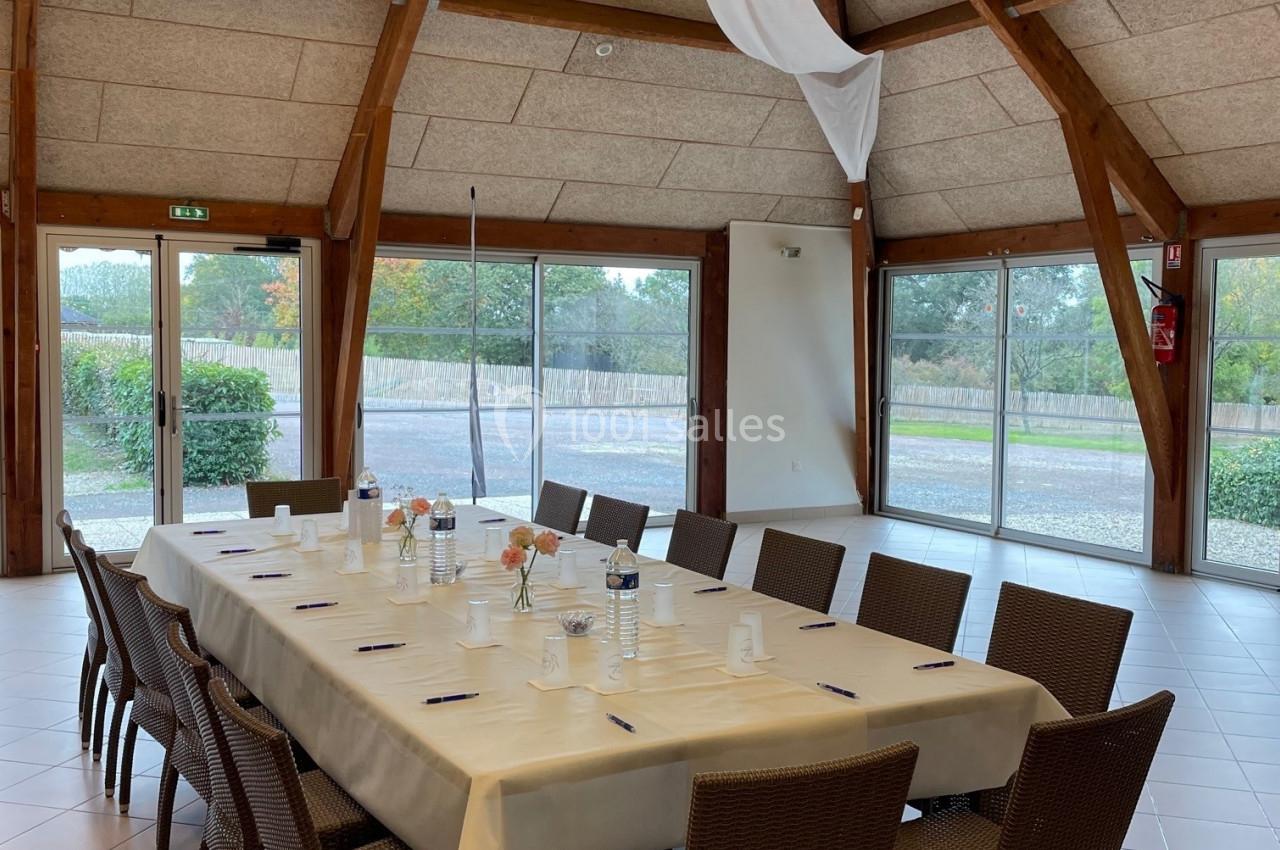 Salle lumineuse avec une grande table rectangulaire dressée, entourée de chaises en rotin, et des baies vitrées donnant sur…