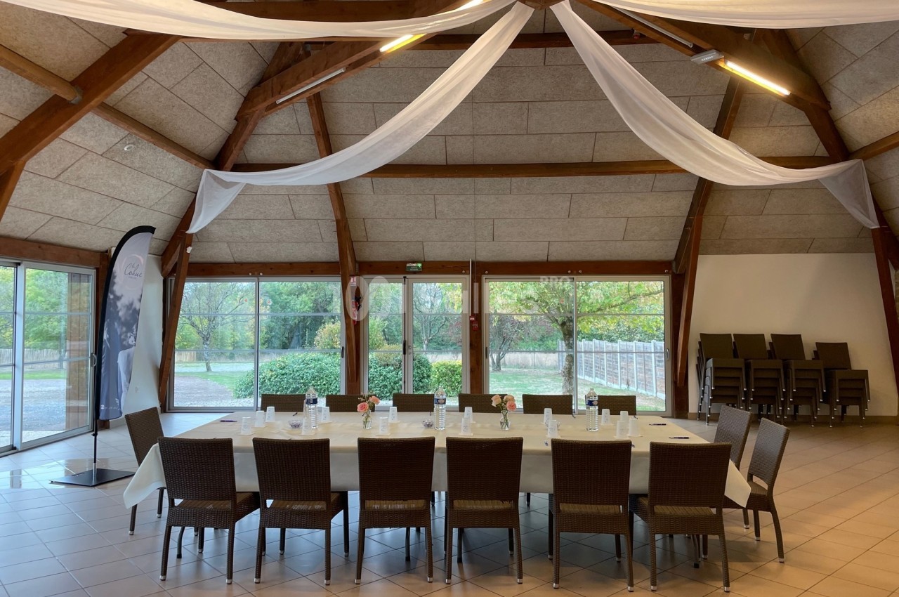 Grande salle lumineuse avec une table rectangulaire dressée pour une réunion, entourée de chaises en bois tressé.