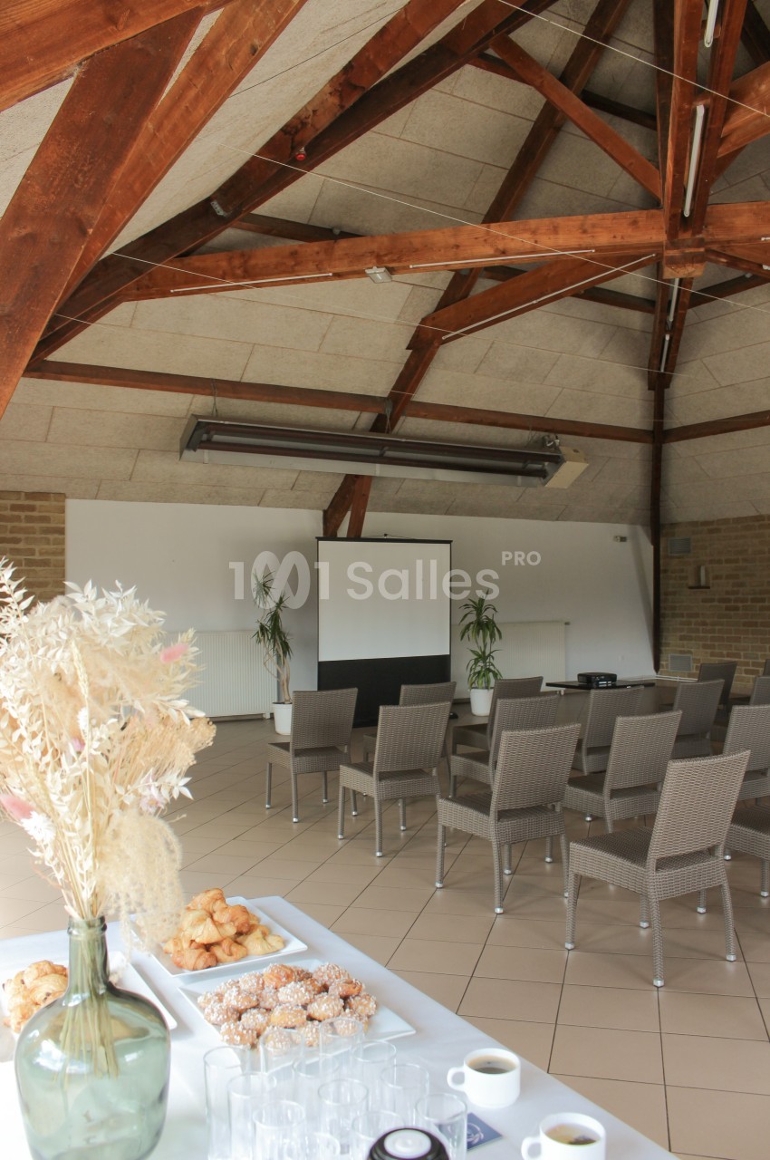 Salle de réunion lumineuse avec chaises alignées face à un écran, table au premier plan avec viennoiseries et boissons.