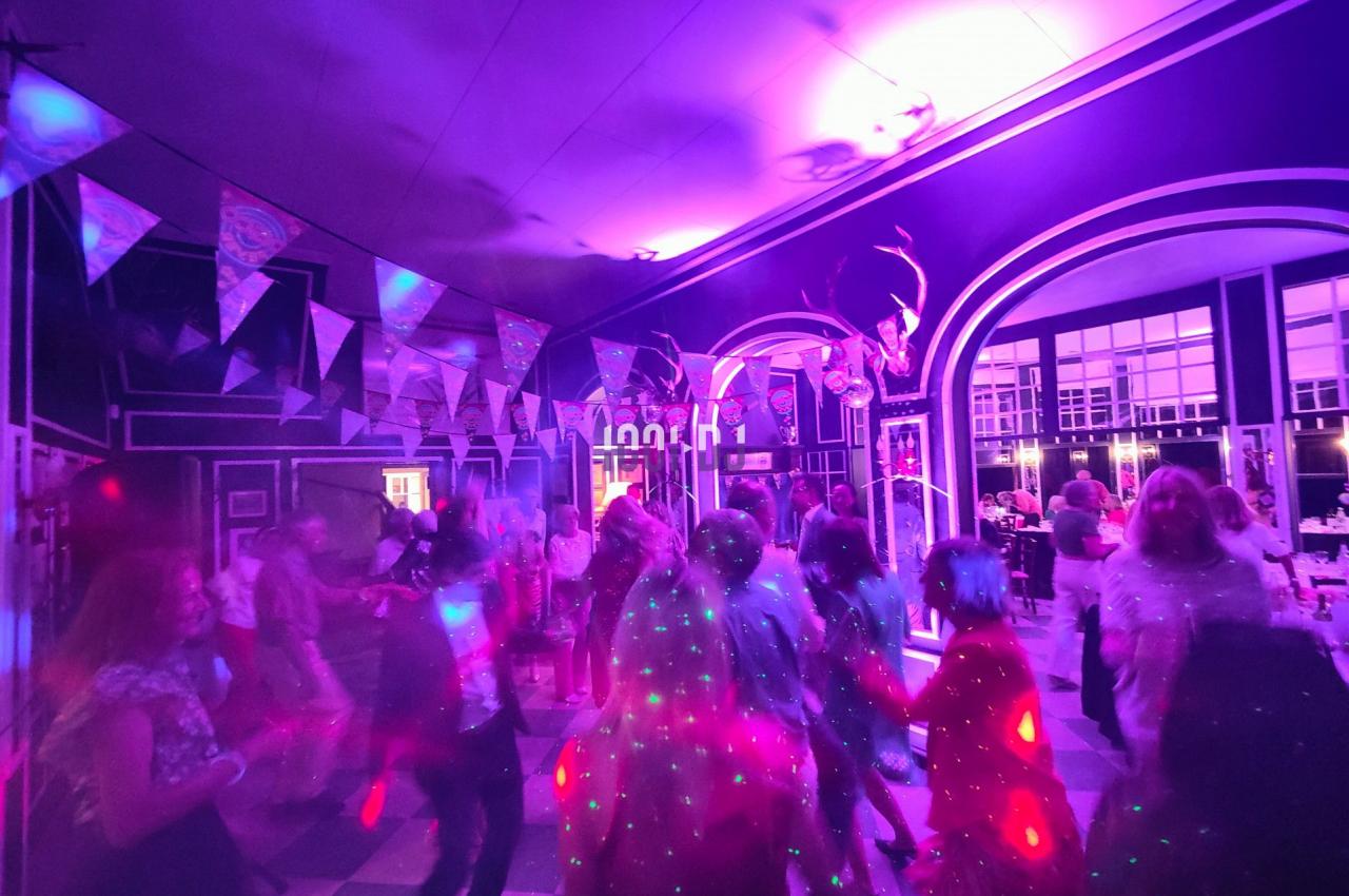 Des personnes dansent sous des lumières colorées dans une salle décorée de guirlandes et d'arches lumineuses.