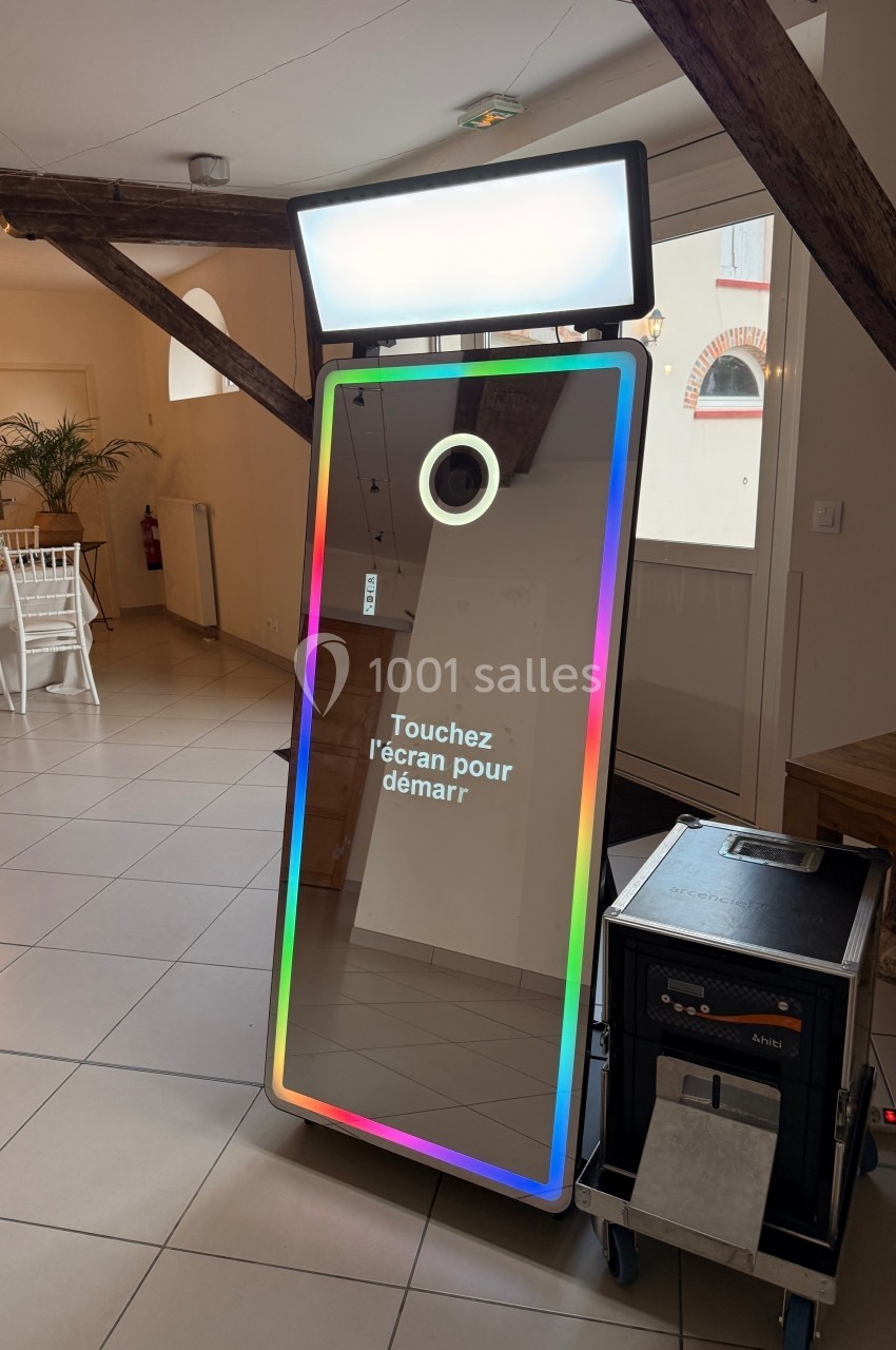 Borne photo interactive avec écran tactile et cadre lumineux, installée dans une salle avec poutres apparentes.