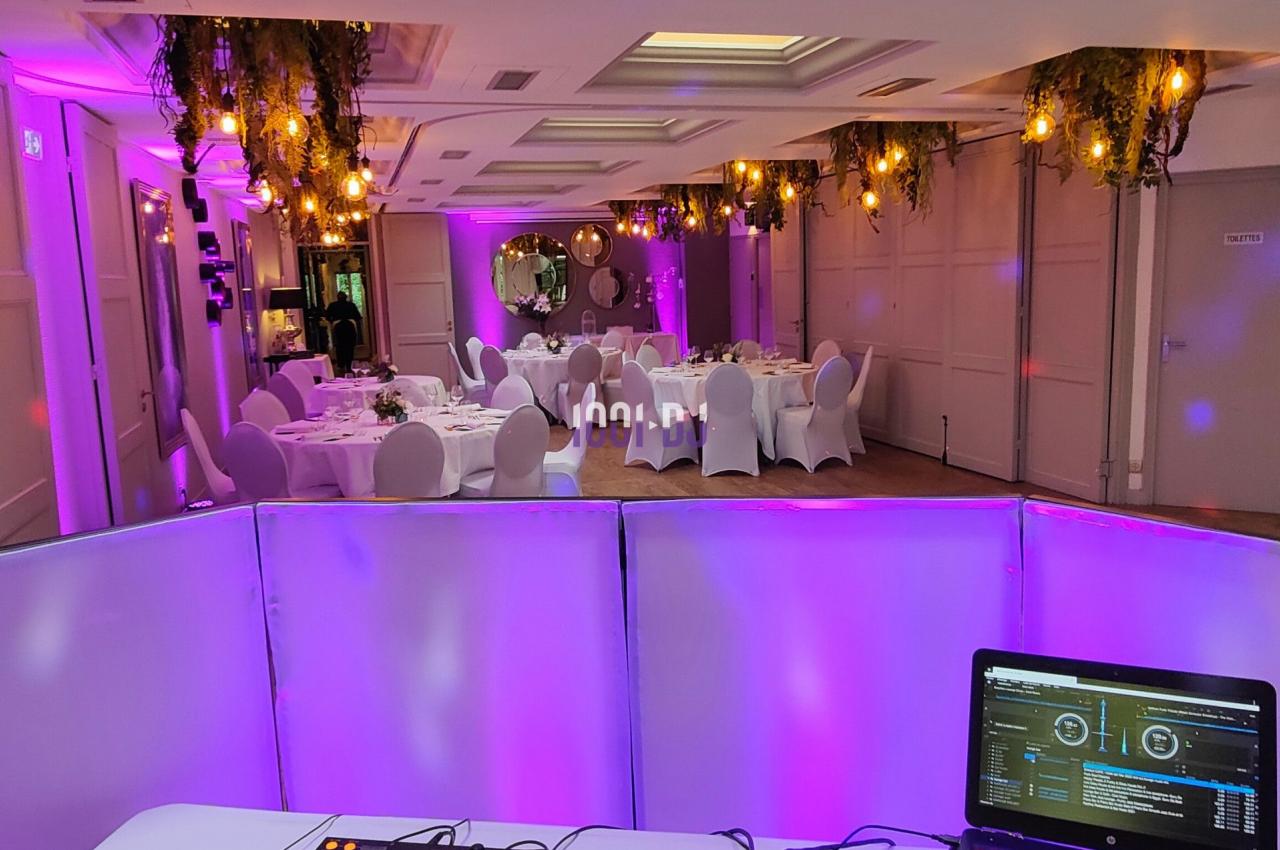 Console de DJ avec ordinateur portable en premier plan, salle de réception décorée et éclairée en violet en arrière-plan.