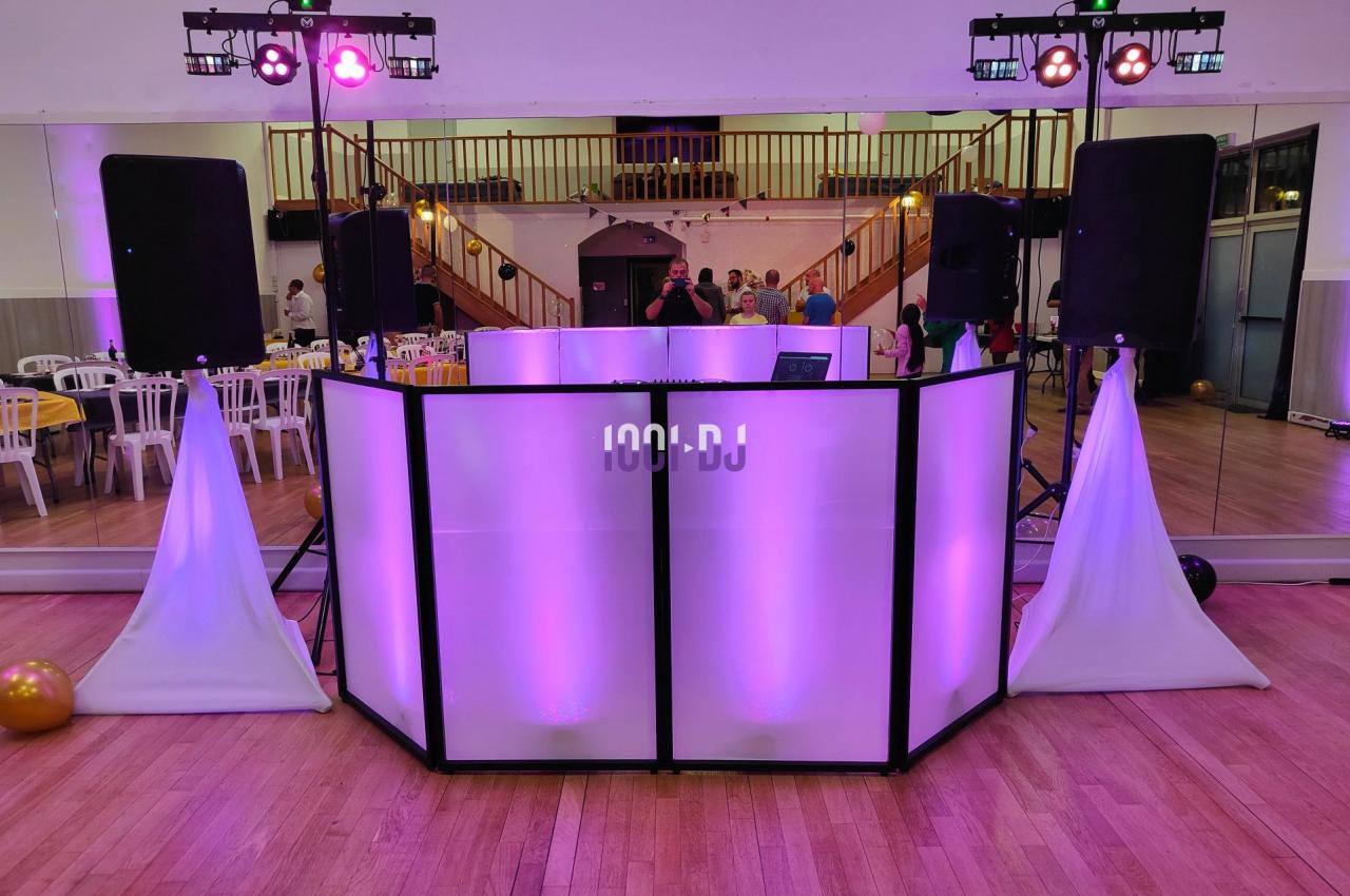 Console de DJ éclairée en violet dans une salle de réception avec des enceintes et des lumières colorées.