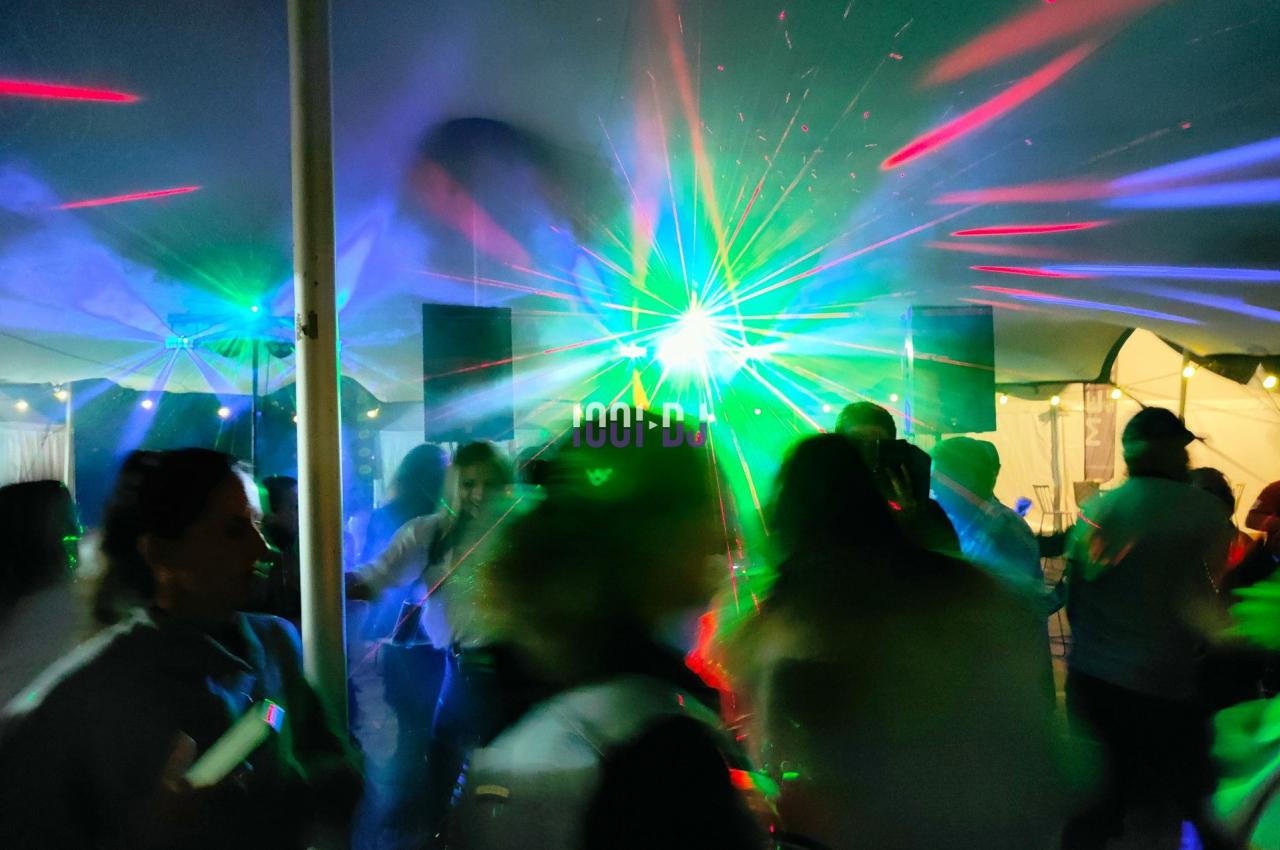 Personnes dansant sous une tente avec des lumières colorées et des effets laser lors d'une soirée festive.