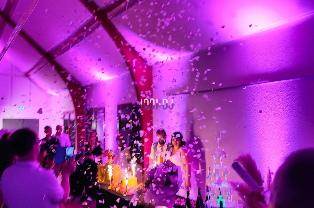 Des confettis tombent dans une salle éclairée de lumières violettes, entourant des personnes célébrant un événement.