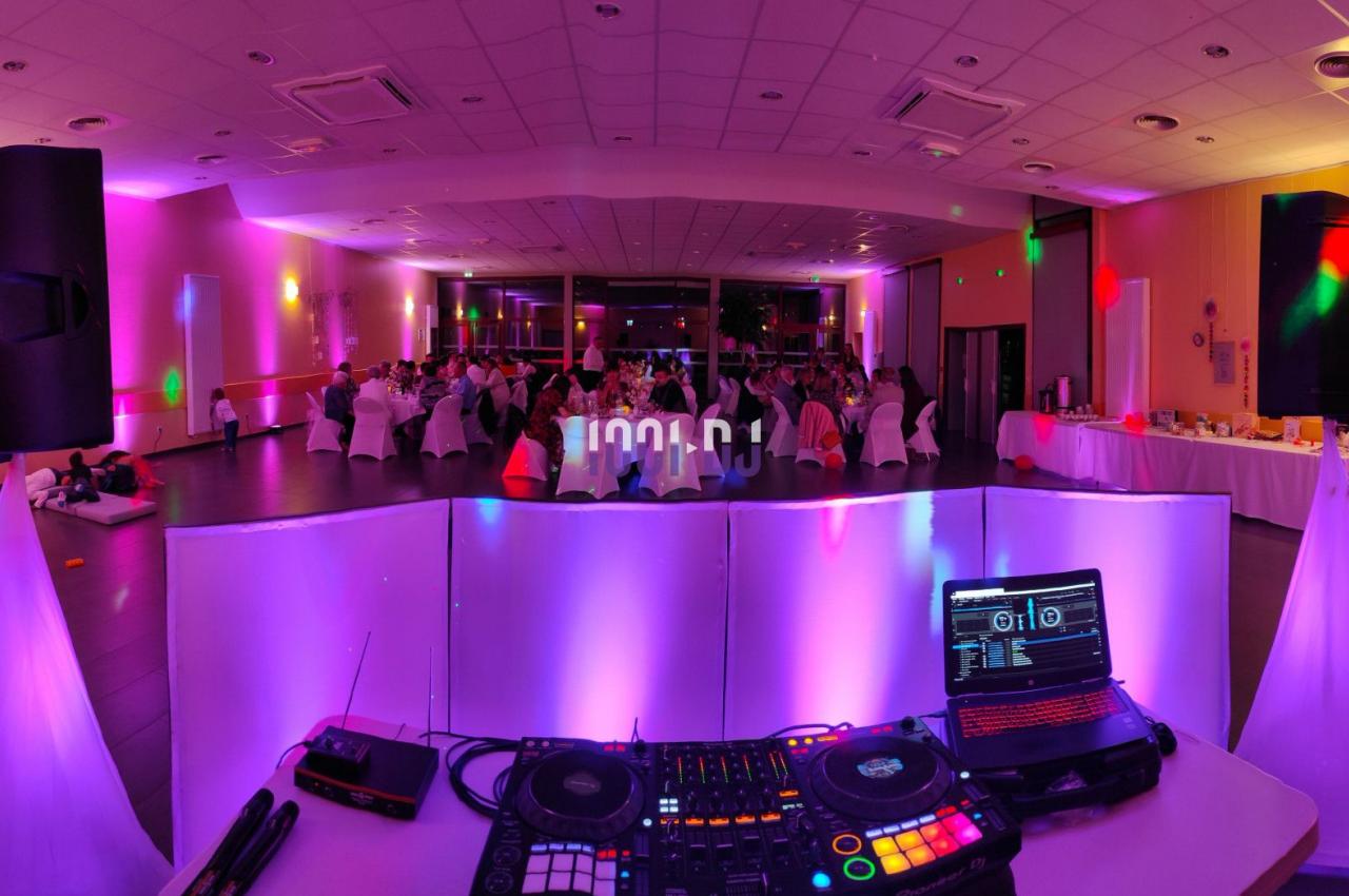 Salle de réception éclairée avec des lumières colorées, vue depuis une table de DJ équipée de matériel audio.