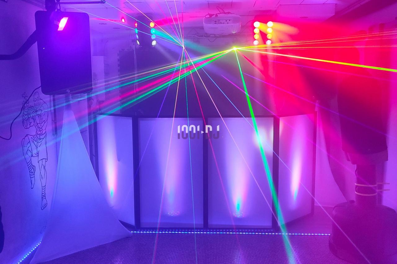 Jeu de lumières colorées et lasers projetés dans une salle sombre avec un espace DJ en arrière-plan.
