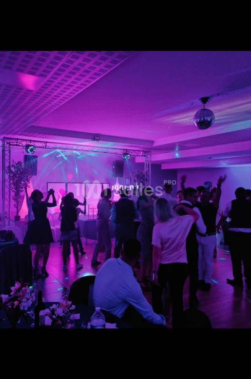 Personnes dansant dans une salle éclairée par des lumières colorées, avec une piste et une ambiance festive.